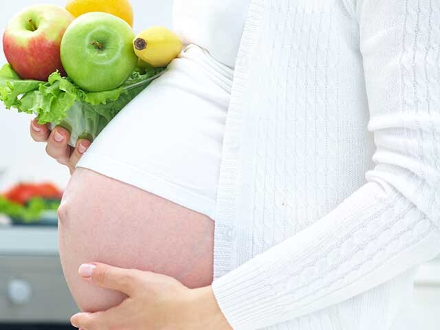 Pregnant woman holding fruits and vegetables