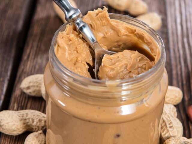 Jar of peanut butter with loose shelled peanuts on brown wood