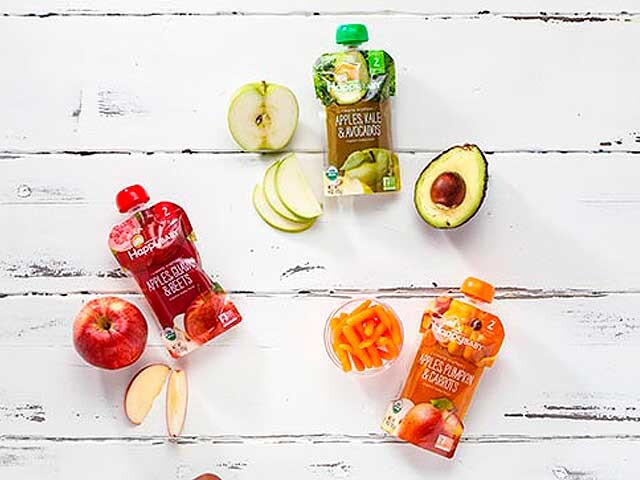 Three bottles Clearly Crafted organic baby food surrounded with fresh fruits and vegetables on white wood