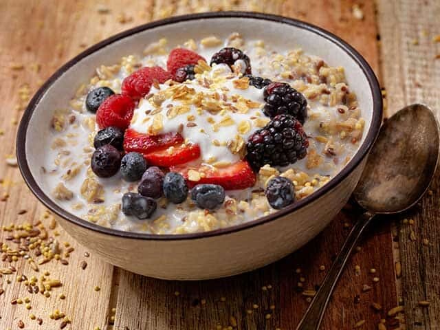 Bowl of oatmeal with berries and spoon on wooden table