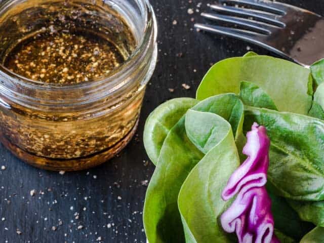 Jar of salad dressing next to salad and fork