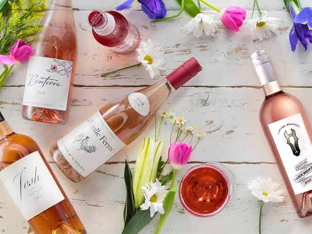 Assorted Bottles of Rose' Wines and flowers on white wood