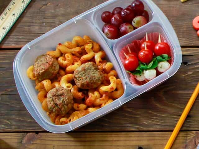 Meal of macaroni and meatballs, veggies and fruit in plastic container