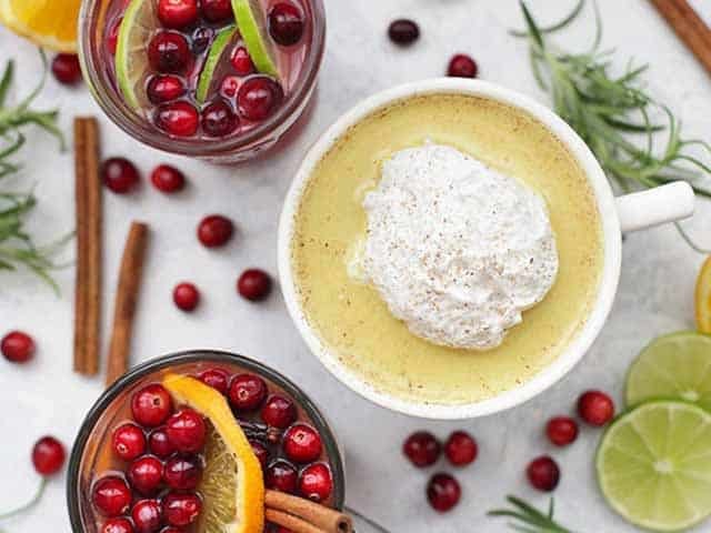 Superfood Holiday Drinks with cinnamon sticks, fruit and herbs laying around the glasses