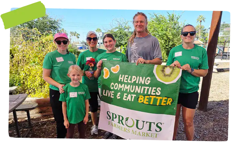 Volunteers holding a banner that says helping communities live and eat better, with sprouts logo
